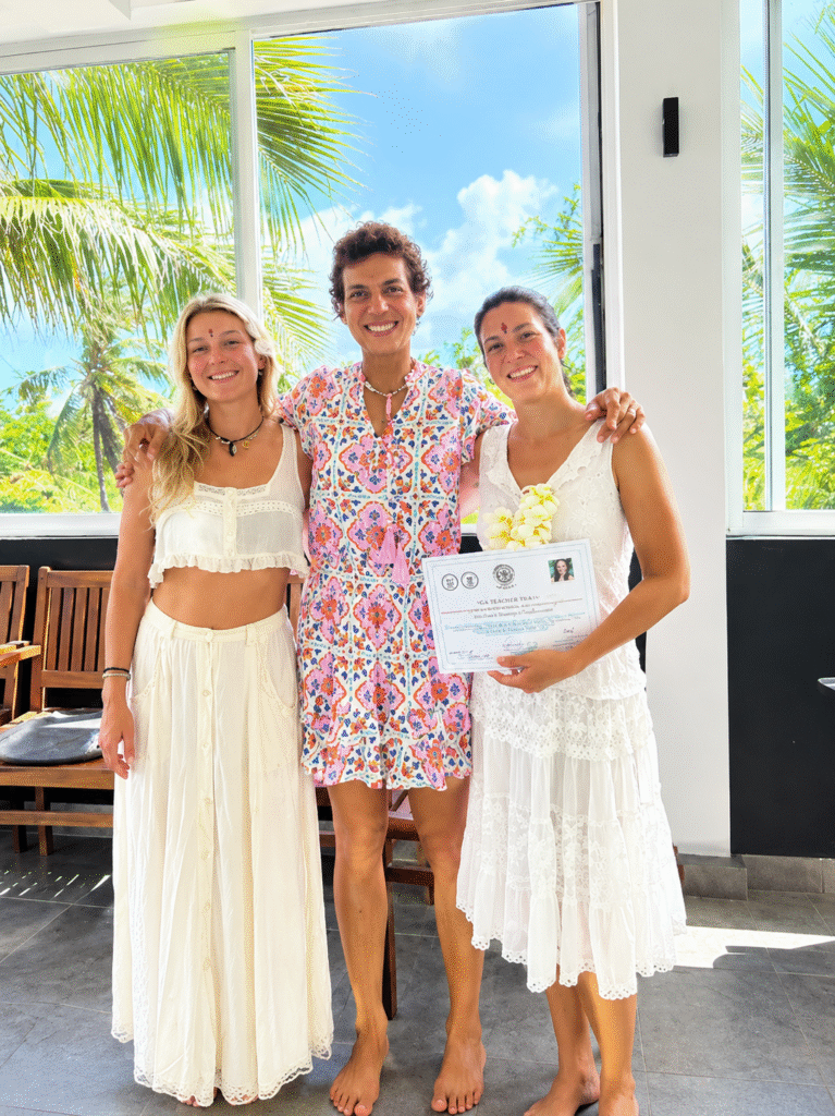 Three yoga graduates celebrating their certification in a tropical studio.